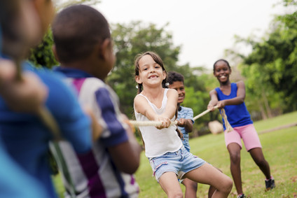Children and recreation, group of happy multiethnic school kids playing tug-of-war with rope in city park. Summer camp fun